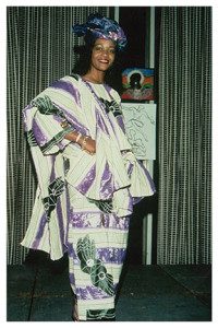 A woman in purple and white dress standing next to a wall.