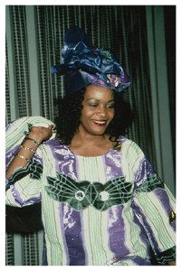 A woman in purple and white dress with blue hat.