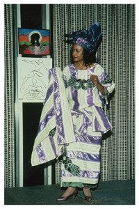 A woman in purple and white dress standing next to a wall.