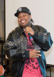 A man in a leather jacket and hat holding a microphone.