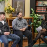 Three people sitting in a room with a woman.