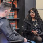 A woman and man are sitting in front of books.