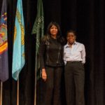 Two women standing in front of a flag.